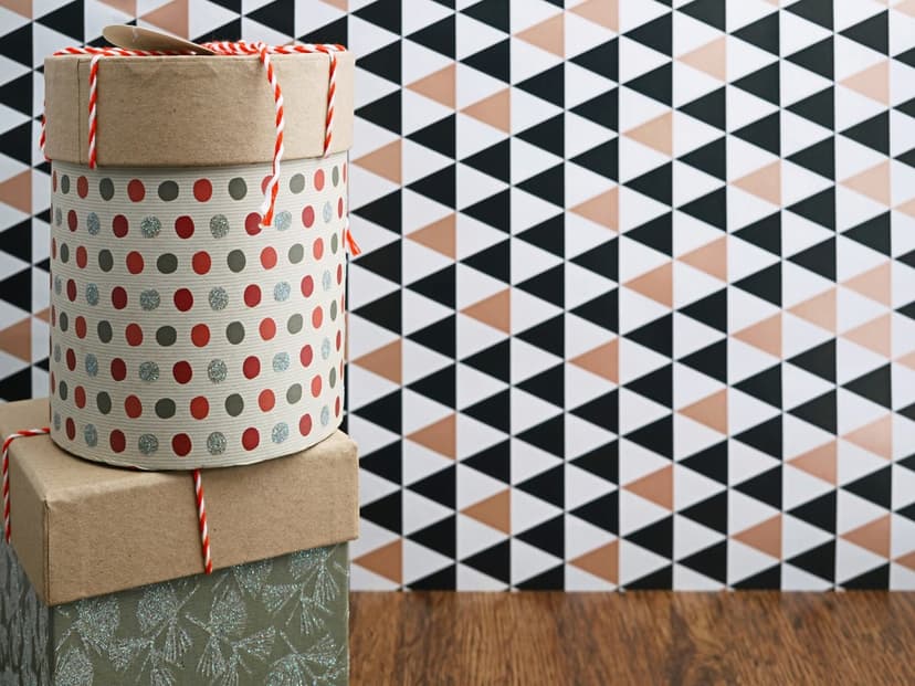 Stacked gift boxes with polka dots and twine sit before a rose gold and black triangle geometric pattern.