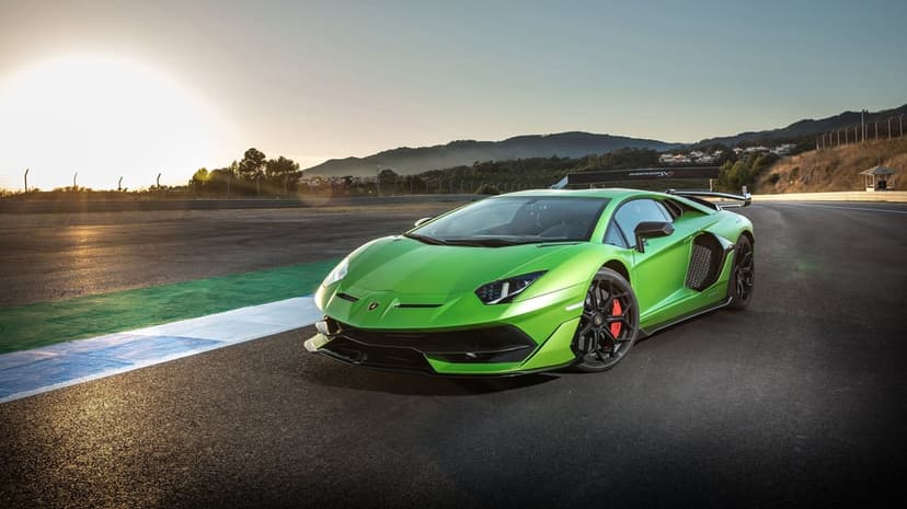 Green Lamborghini Aventador SVJ on a race track at sunset with mountains and a clear sky in the background.