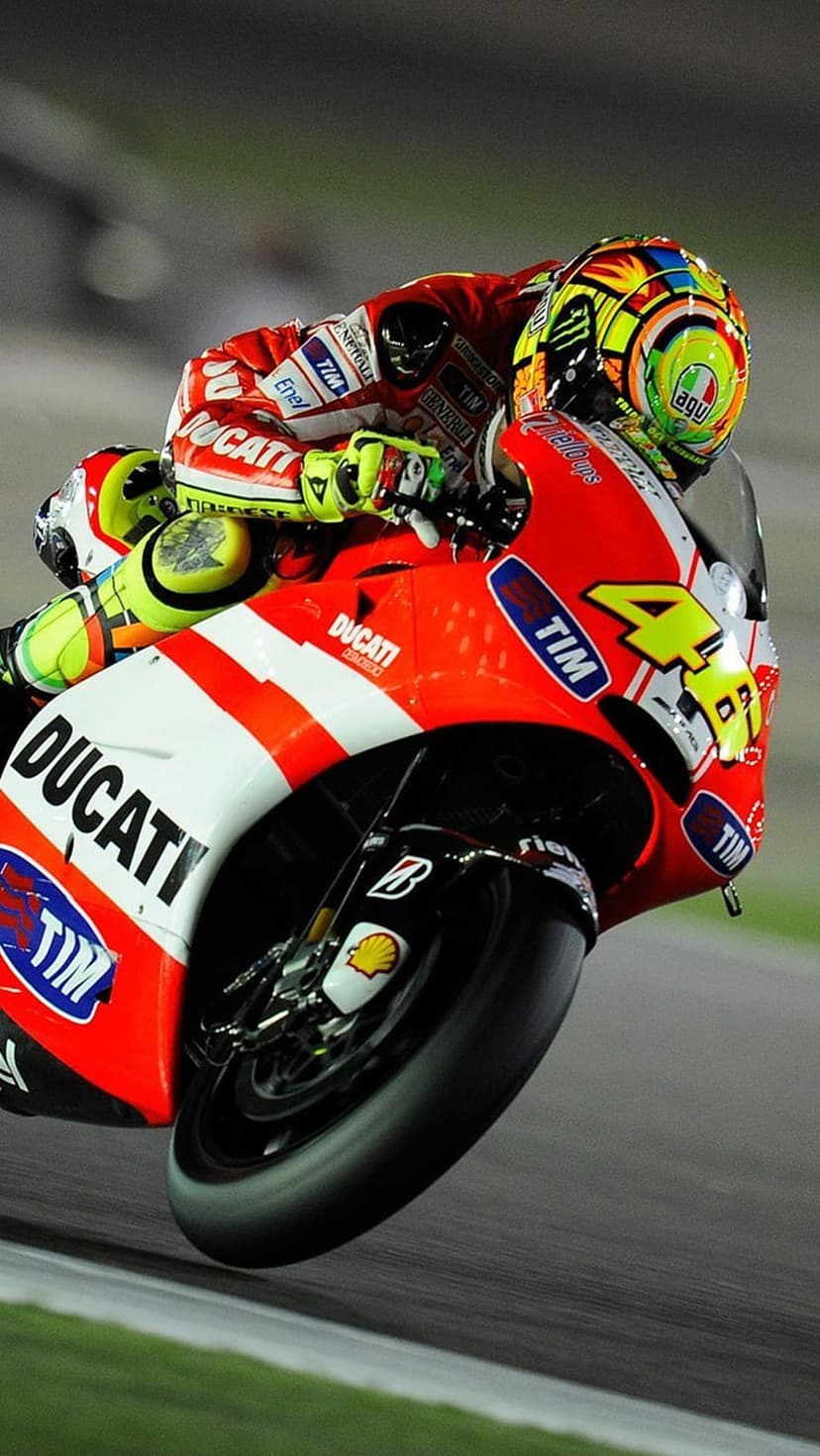 Valentino Rossi on a red Ducati MotoGP bike with number 46 leaning deep into a racetrack corner during a race.