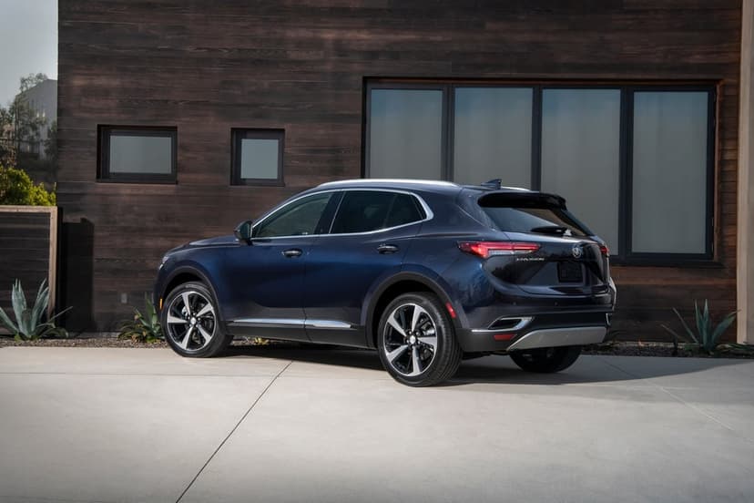 Dark blue Buick Envision SUV parked on a concrete driveway in front of a modern wood-paneled house under bright sun.