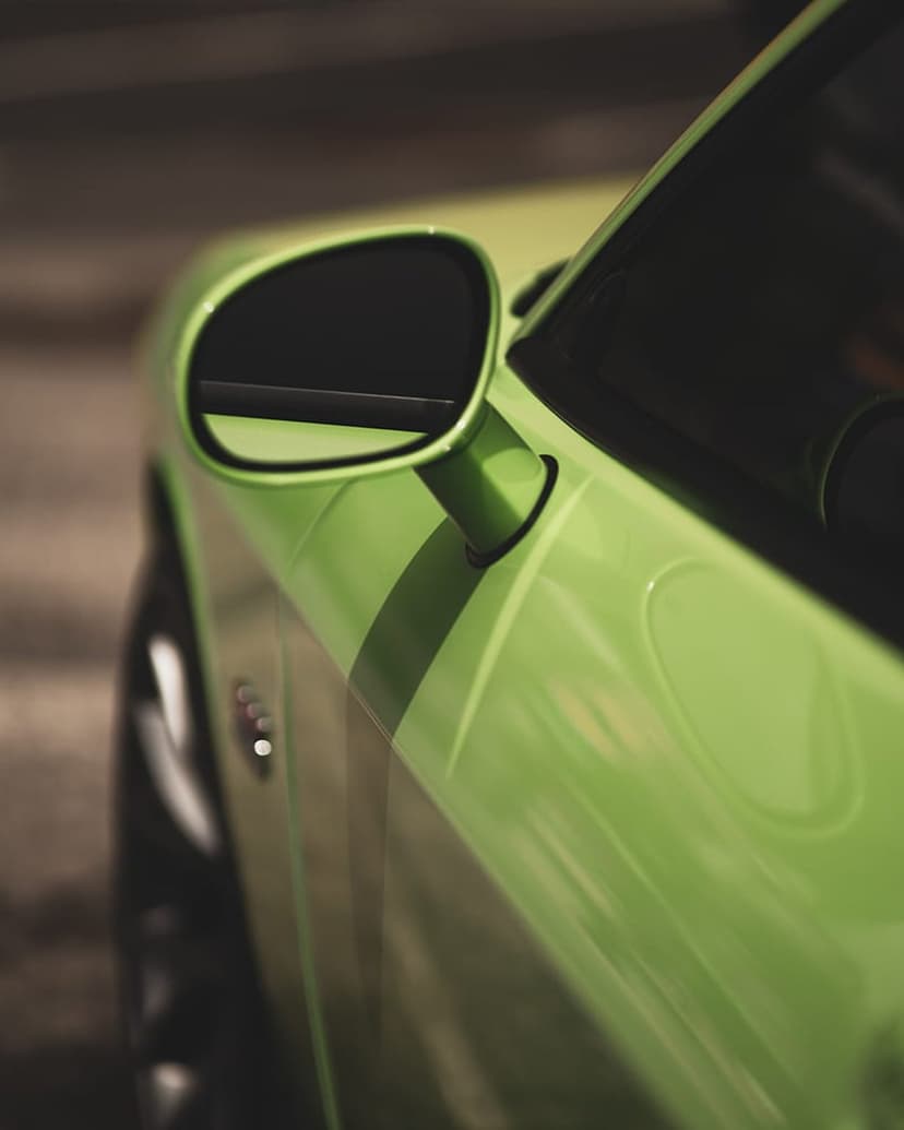Glossy lime green car fender with a white racing stripe and a reflective side mirror showing blurred scenery.
