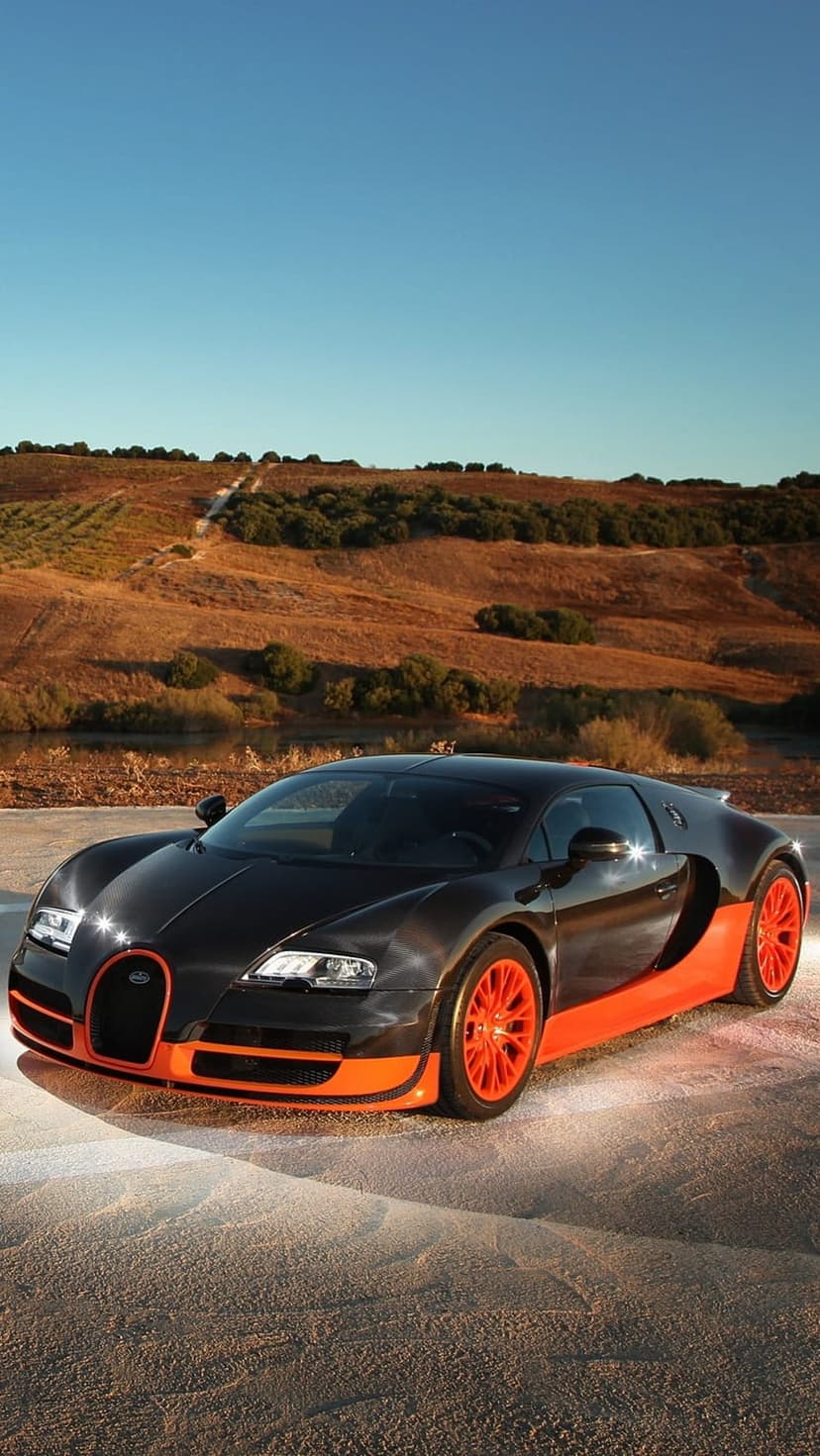 Black Bugatti Veyron with orange accents parked on sand dunes under a clear blue sky in a desert landscape.