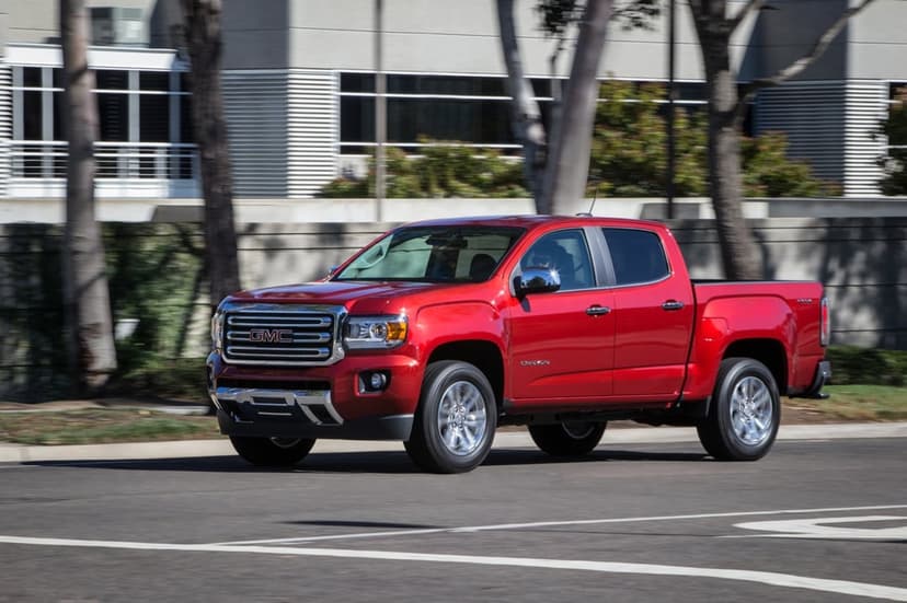 Metallic red GMC Canyon pickup truck driving on a suburban road with motion blur and chrome accents.