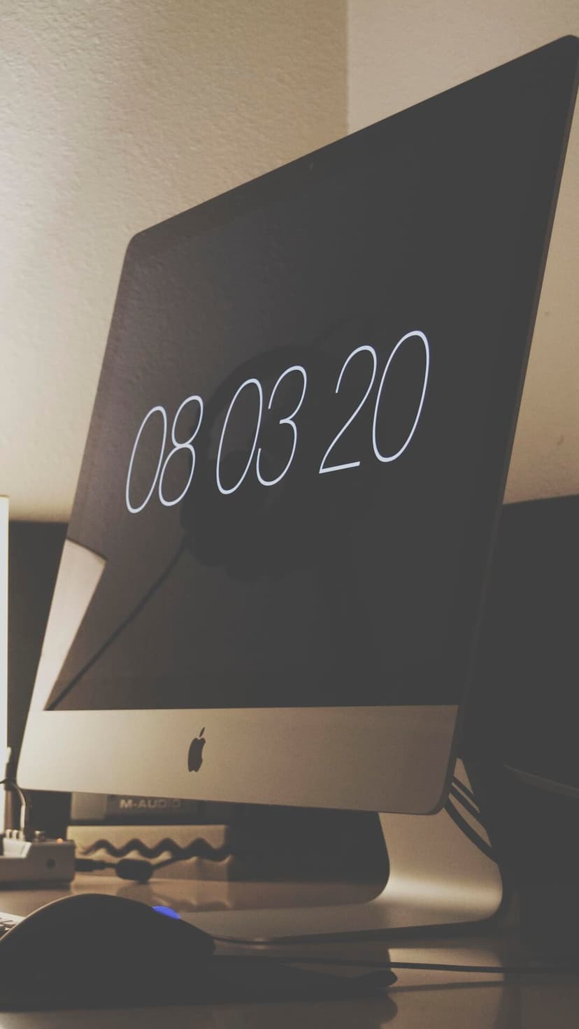 Apple monitor screen with white date numbers 08 03 20 on a dark display in a softly lit office workspace.