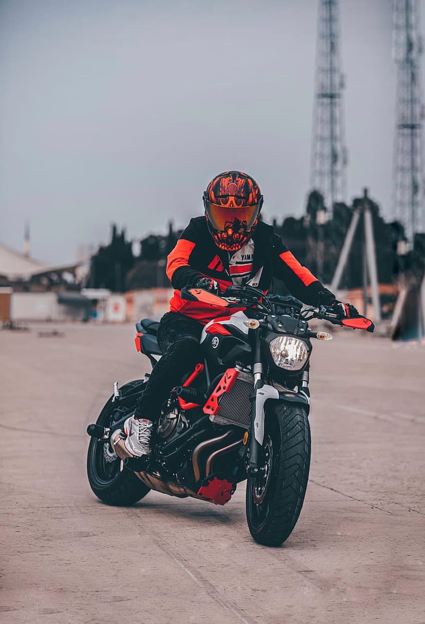 Motorcyclist in orange and black riding gear sits on a Yamaha motorcycle against an industrial urban backdrop.