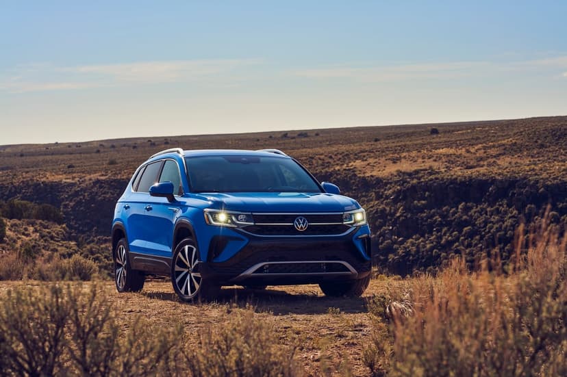 Blue SUV on a dusty trail overlooking a wide desert canyon under a bright afternoon sky with warm lighting.