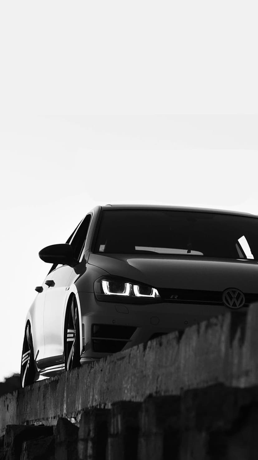 Volkswagen Golf GTI headlights illuminate a textured concrete wall in a low-angle black and white composition.