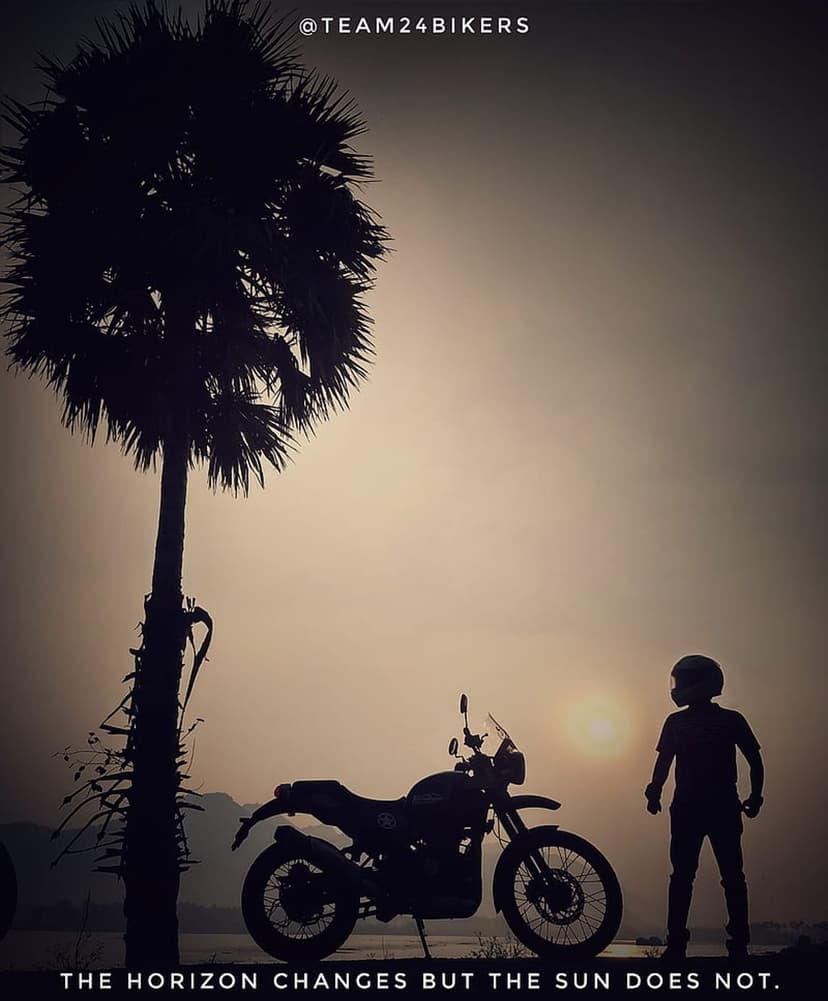 Motorcyclist silhouette beside a palm tree against a vibrant orange and yellow sunrise on a coastal horizon.