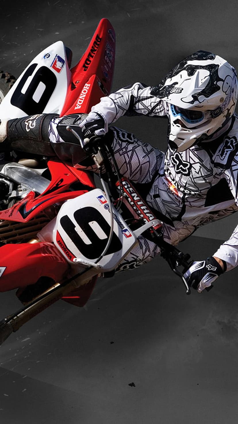 Motocross rider in black and white gear jumps a red and white Honda dirt bike with number six decals mid-air.