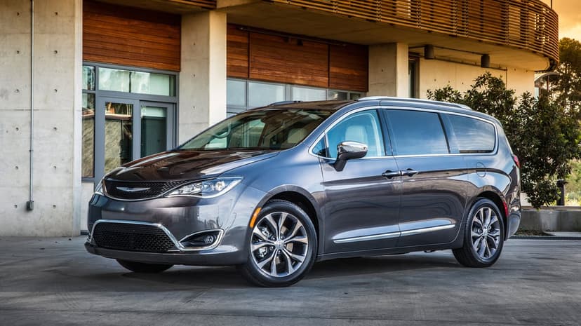 Charcoal Chrysler Pacifica minivan parked in front of a modern concrete and wood building during daylight.