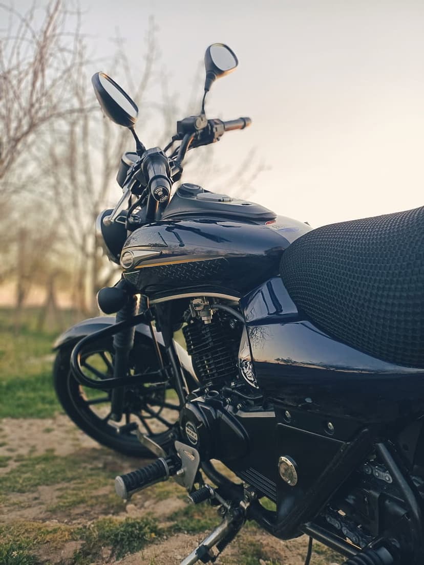 Dark blue cruiser motorcycle featuring chrome engine parts and a black seat against a blurred twilight park backdrop.