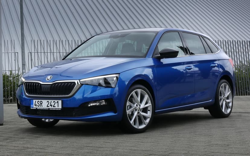 Blue Skoda Scala hatchback parked on a paved surface against a modern metallic wall in daylight.