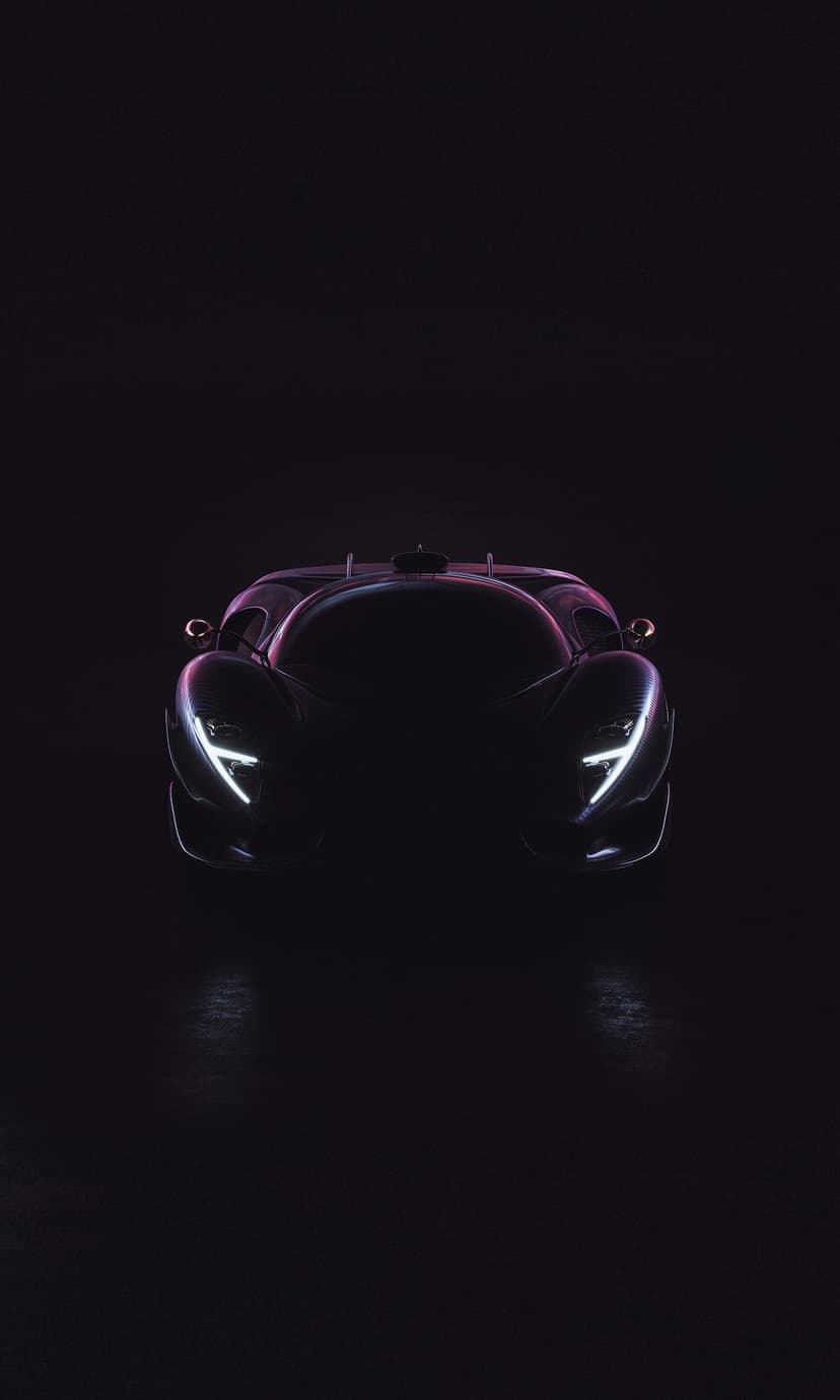 Front of a dark supercar with glowing white LED headlights and purple neon light reflections on its black paint.