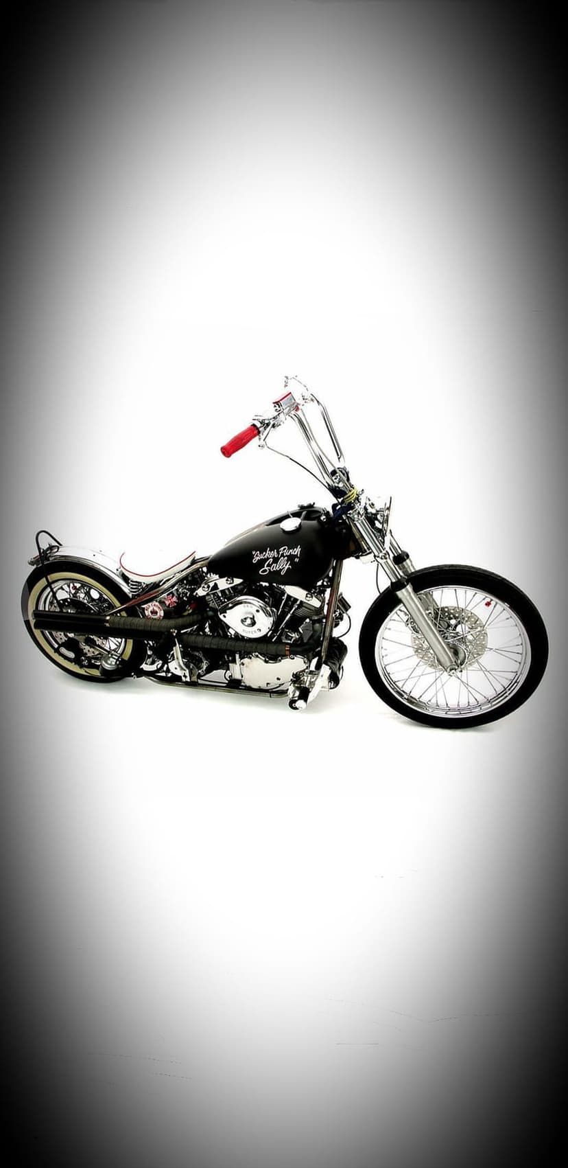 Custom black motorcycle with red handlebars and chrome details rests against a white vignette studio backdrop.
