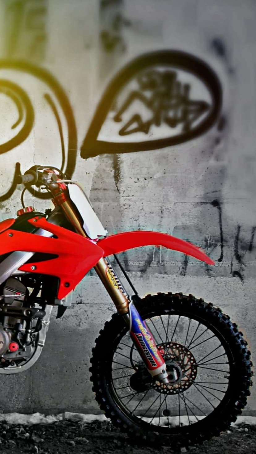 Red motocross bike front wheel and suspension parked in front of a colorful graffiti wall with urban street art.