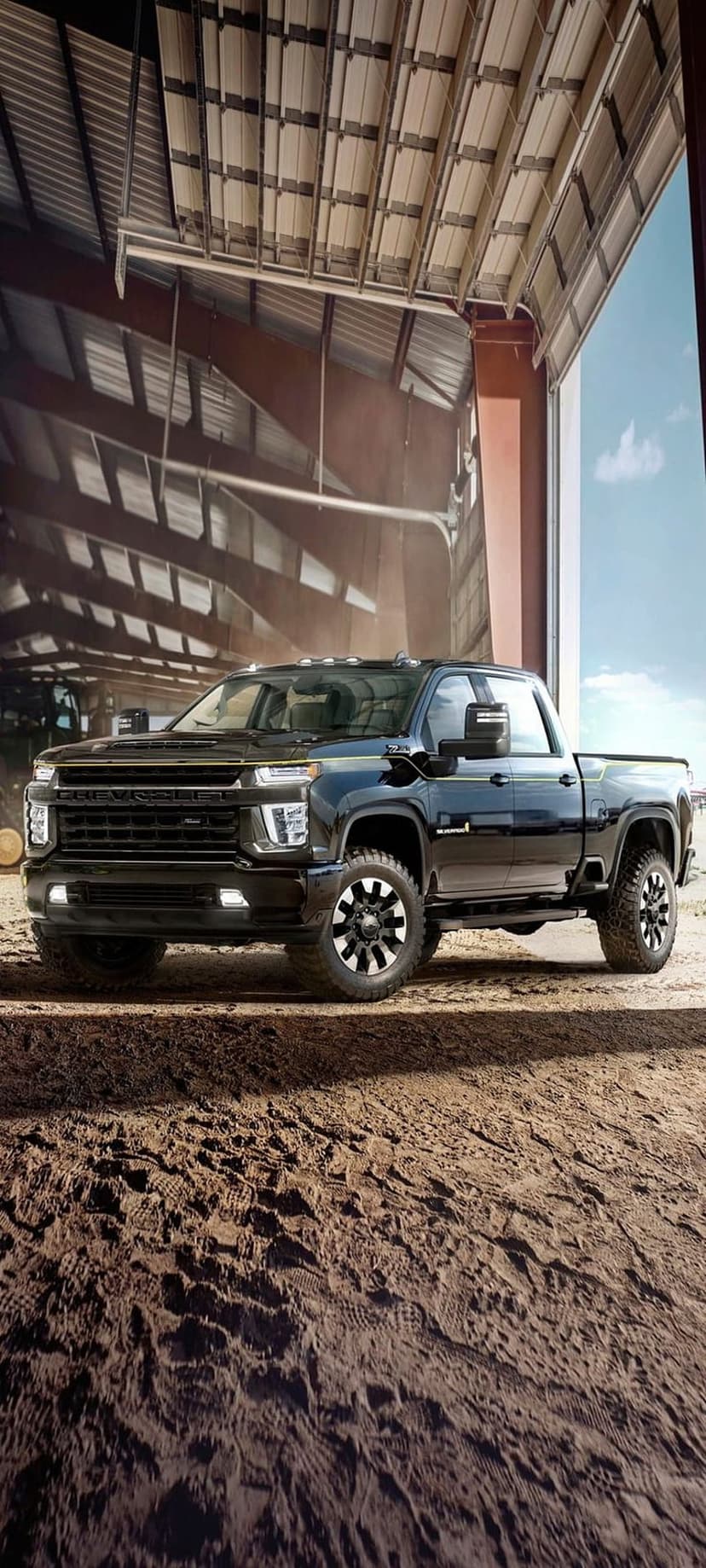 Black Chevrolet Silverado HD truck with chrome accents and alloy wheels parked in a sunny industrial dirt lot.