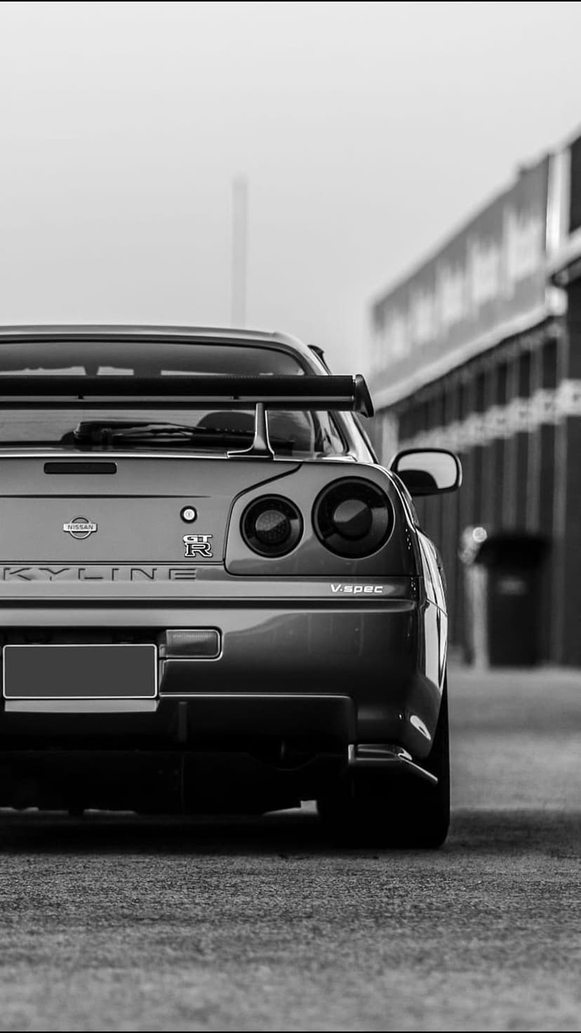 Nissan Skyline GT-R R34 V-Spec rear view features quad taillights and a large wing on dark asphalt.