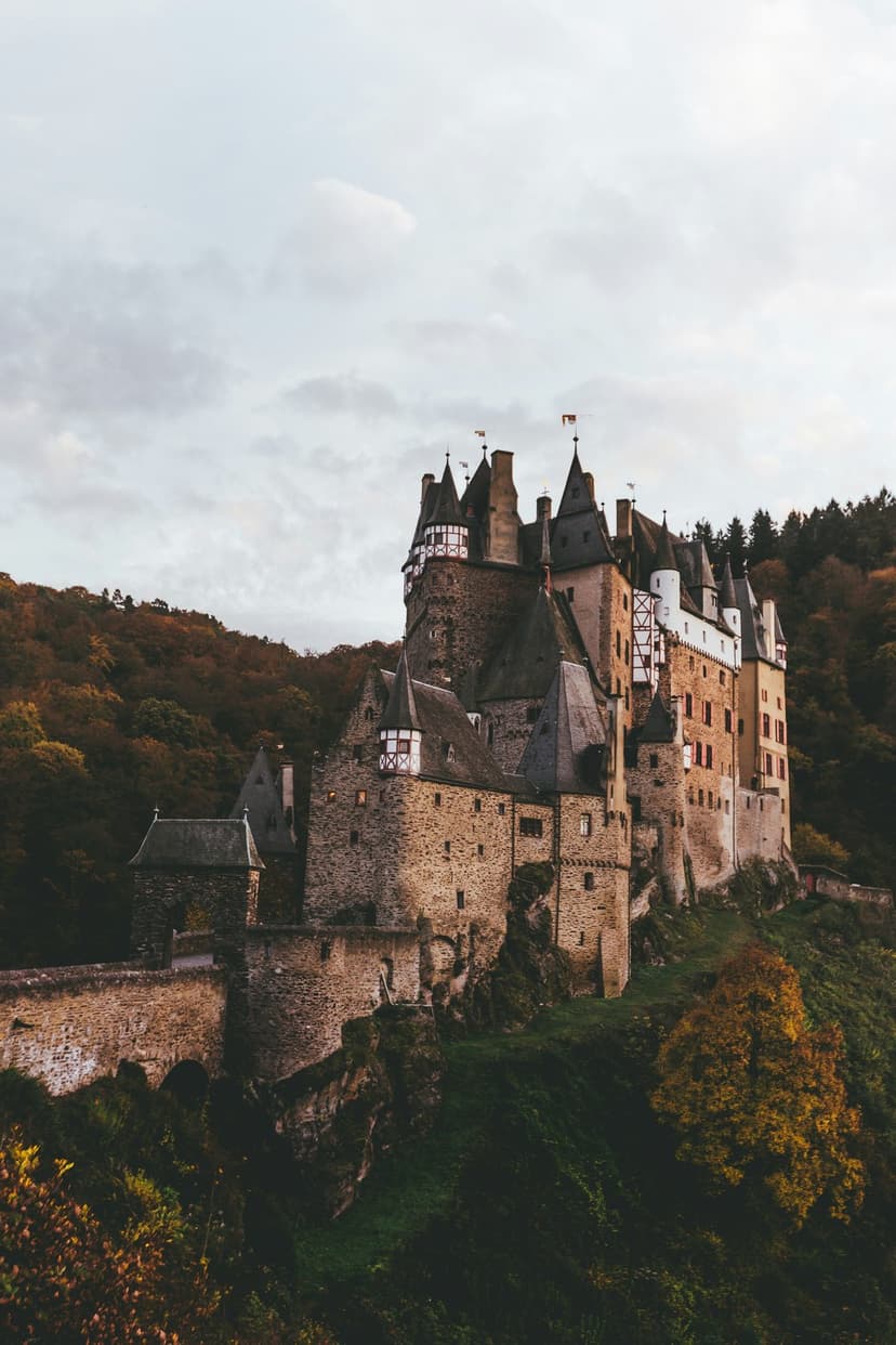 Burg Eltz stone towers and half-timbered walls rise above a dense forest of vibrant red and orange autumn trees.