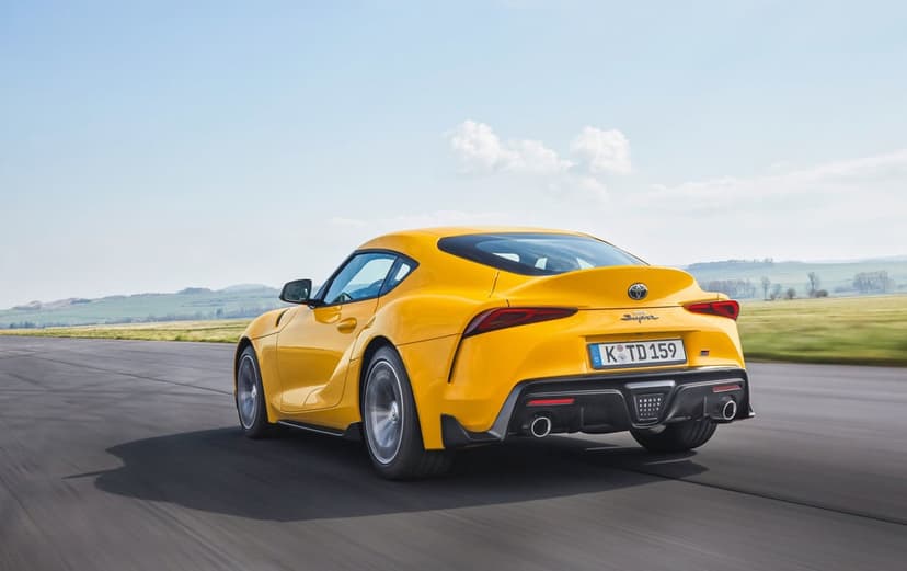 Rear view of a yellow sports car driving fast on an asphalt road under a bright blue sky with soft white clouds.