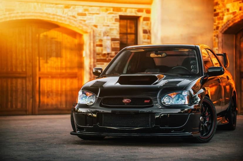 Modified black Subaru WRX STI parked in front of a stone building during golden hour with warm sunset lighting.