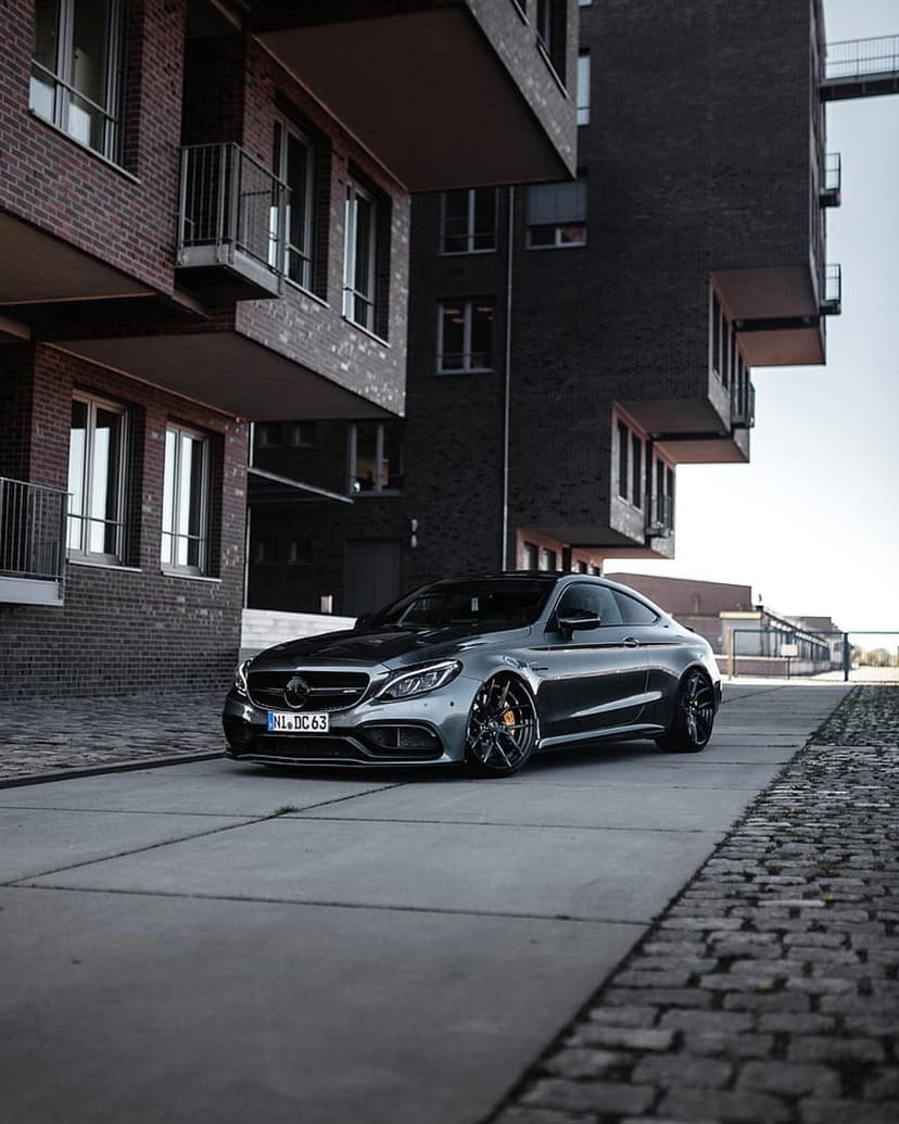 Mercedes-AMG C63 Coupe with black wheels parked on concrete near brick buildings in a vertical urban composition.