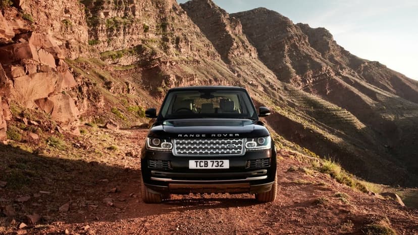 Front view of a black Range Rover SUV parked on a dusty mountain road with layered red rock formations behind it.