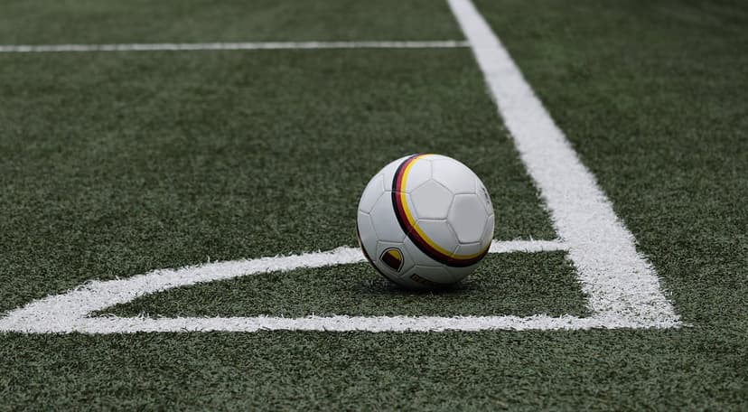 Soccer ball with colorful stripes sits on green artificial turf at the junction of two white boundary corner lines.