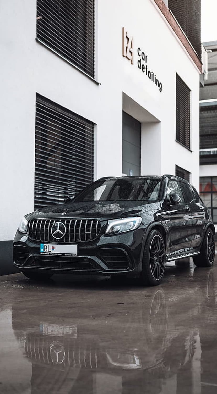 Black Mercedes GLC AMG SUV sits on rain-slicked pavement with water droplets and mirror-like ground reflections.