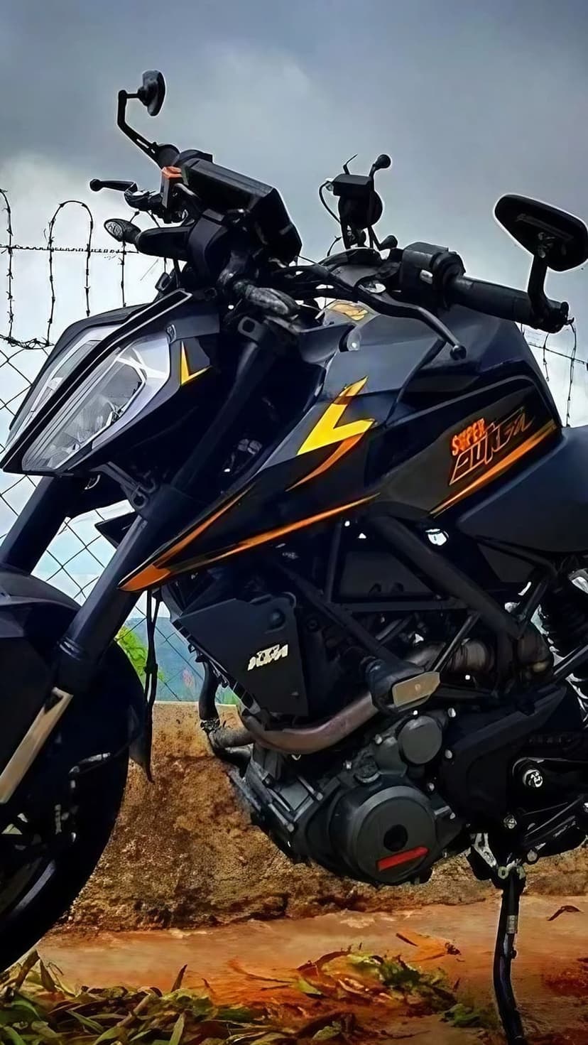 Black KTM Super Duke motorcycle with orange accents parked by a barbed wire fence against a cloudy backdrop.