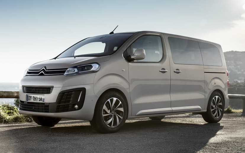 Silver Citroen SpaceTourer van parked on an asphalt road with a coastal hill background under a clear sky.
