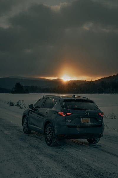 Mazda CX-5 drives through snowy landscape at sunset