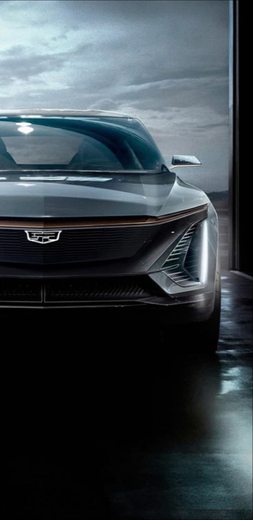 Cadillac Lyriq front grille with vertical LED lights and a glowing emblem on a dark reflective wet surface.