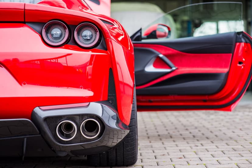 Red Ferrari rear view showing circular taillights, dual exhausts, and an open door revealing a luxury interior.