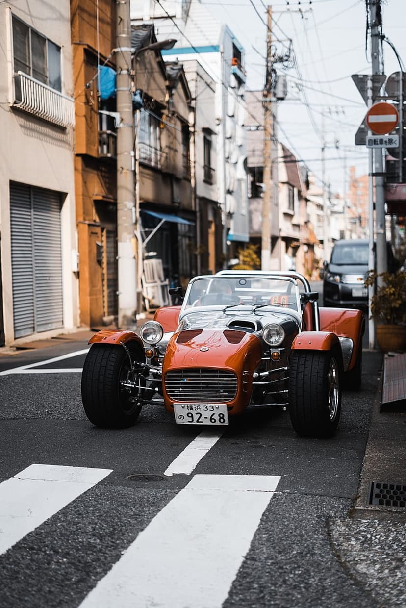 Orange vintage sports car with chrome accents parked on a Japanese pedestrian crossing between city buildings.