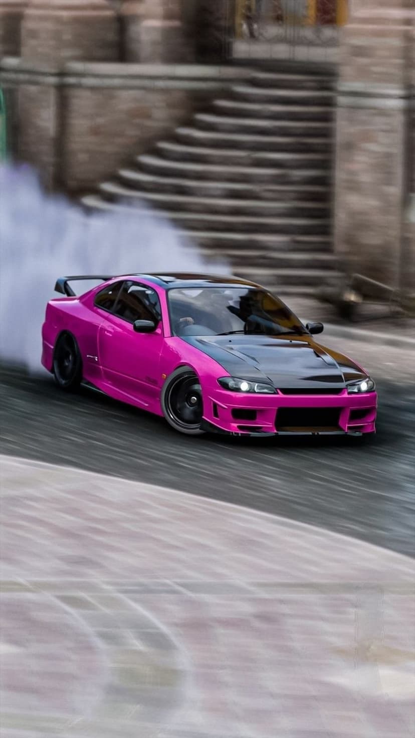 Pink Nissan Silvia S15 drifts with tire smoke, featuring a black carbon fiber hood and large rear spoiler.