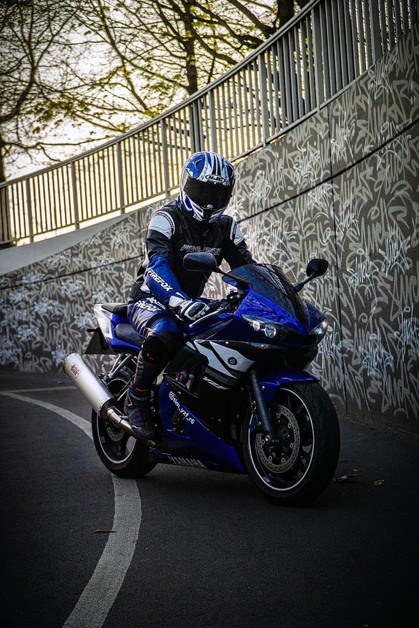 Motorcyclist in blue gear on a Yamaha sportbike parked in front of a concrete wall with black and white graffiti.