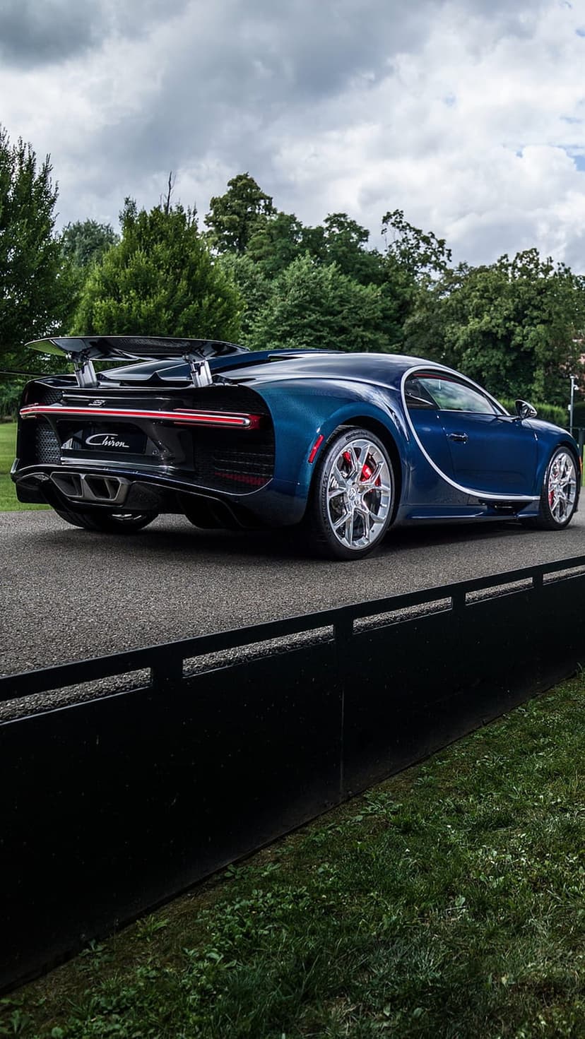 Blue Bugatti Chiron rear view showing the active wing, red brake calipers, and tail lights on a paved road.