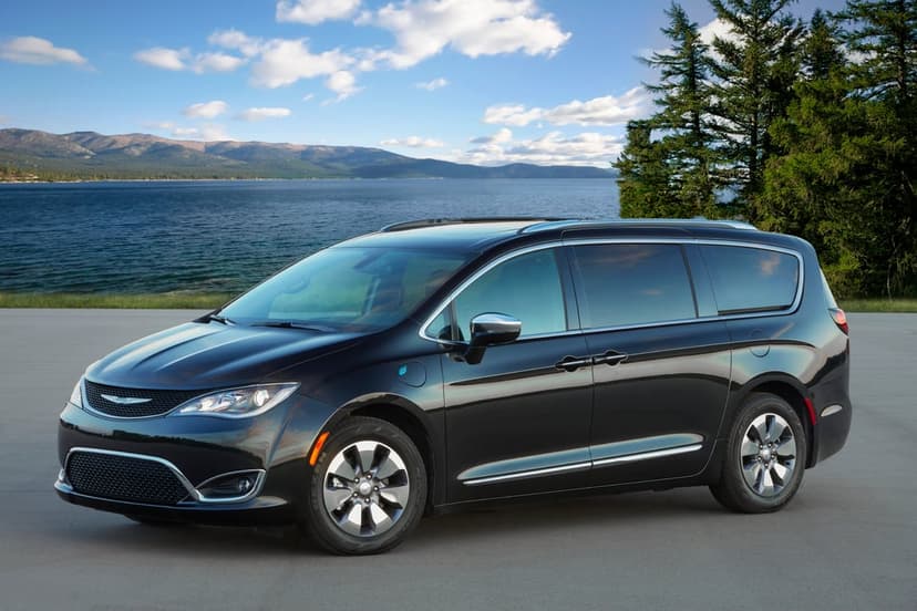 Black Chrysler Pacifica Hybrid parked on a road beside a blue lake with distant mountains and a clear sky.