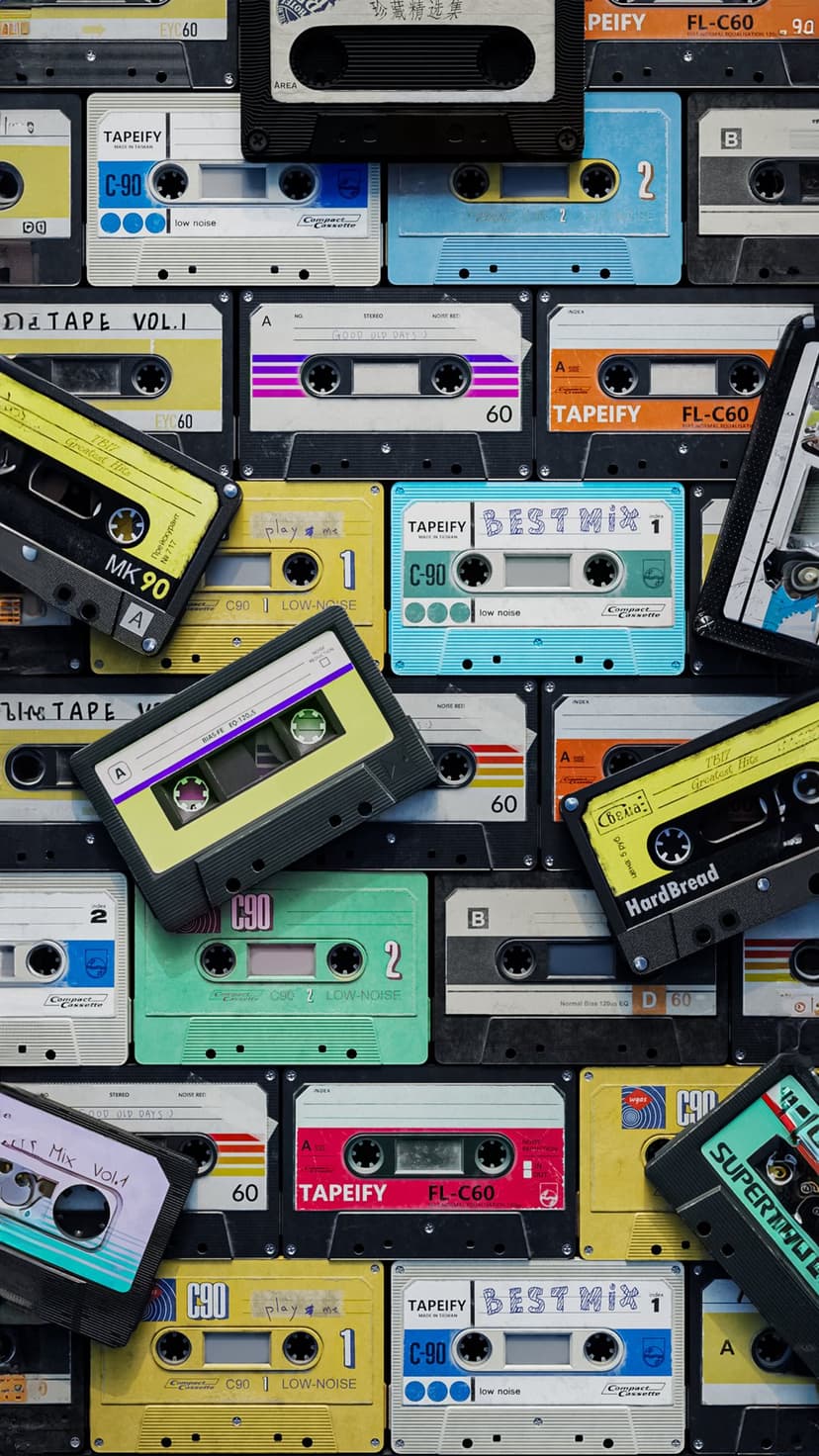Colorful retro cassette tapes with handwritten labels are stacked in a dense, nostalgic music collection.