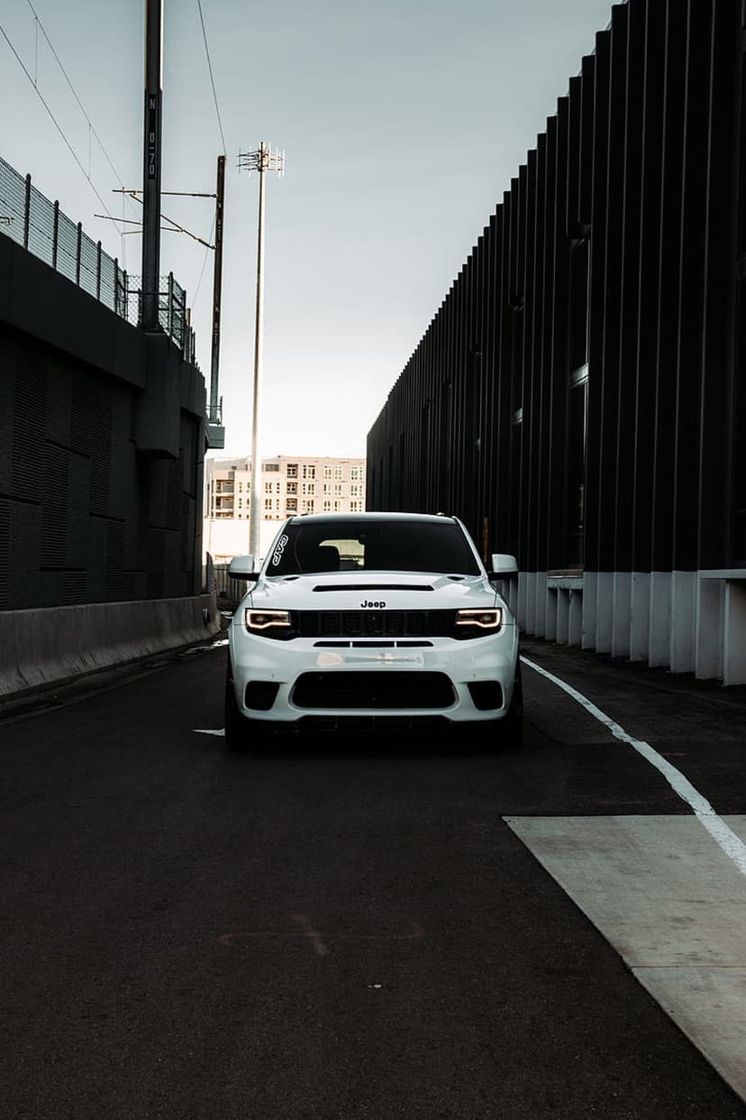 White Jeep Grand Cherokee SRT with glowing headlights parked on a dark urban street beside a modern building.