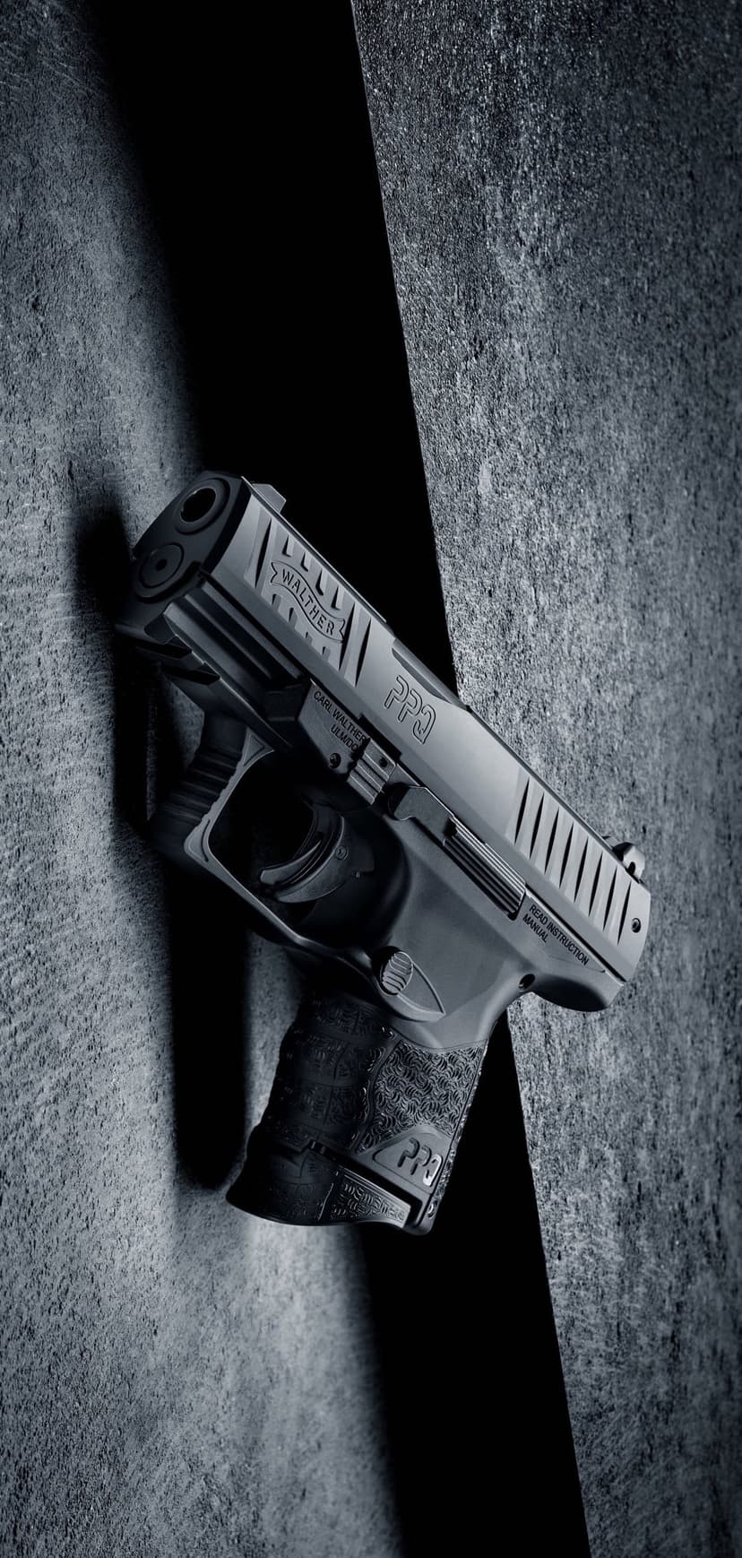 Walther PPQ handgun with a textured grip resting against a gray concrete wall with strong shadow highlights.