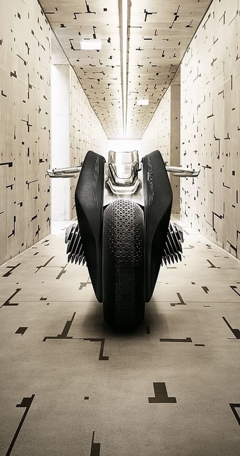 Matte black concept motorcycle stands in a corridor of abstract geometric patterns with intricate tire detailing.