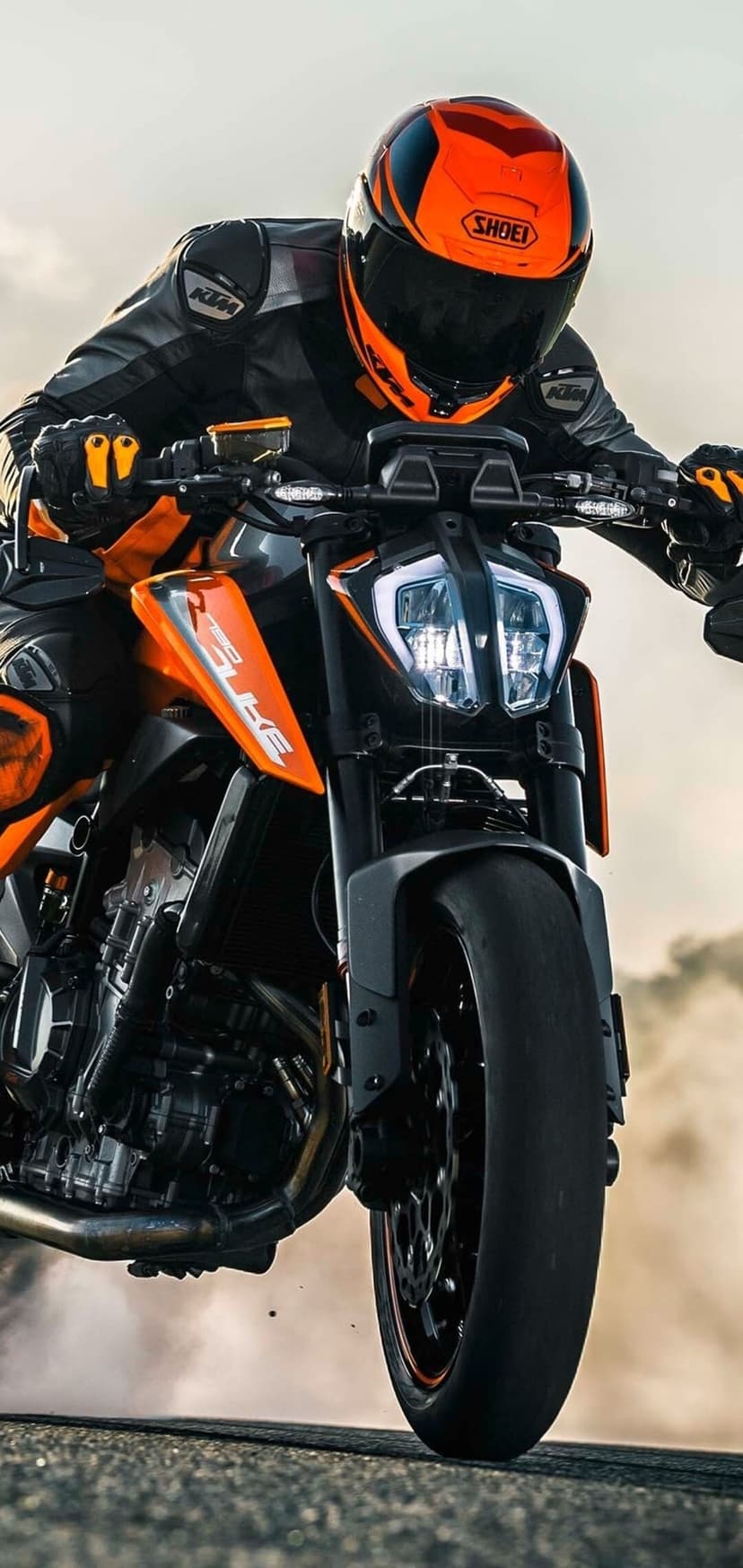 Rider on an orange and black KTM motorcycle leaning forward during a high-speed stunt on a paved track.