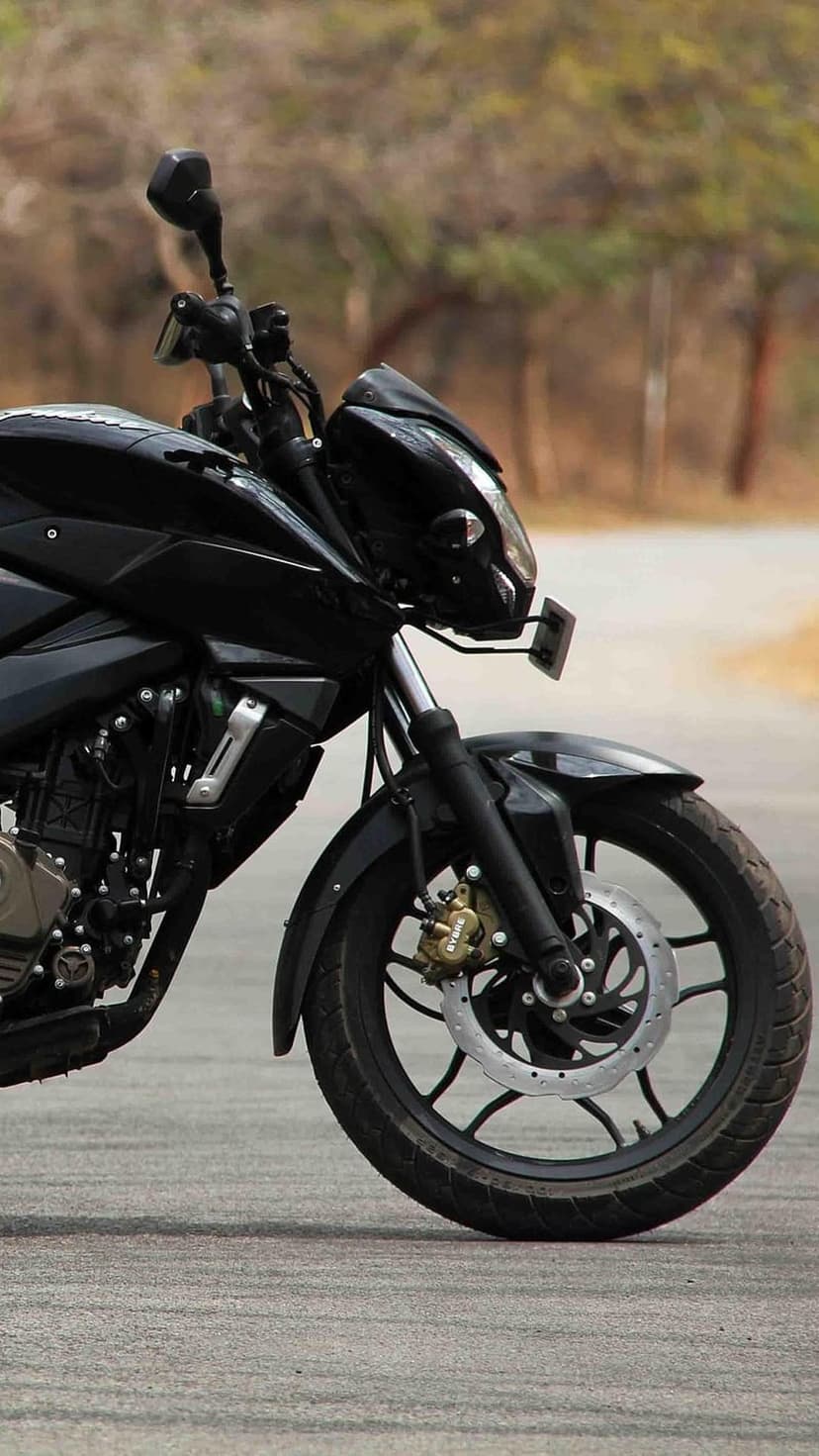 Black sport motorcycle with visible front disc brakes and suspension parked on an asphalt road with blurred trees.