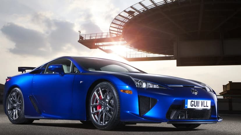 Blue Lexus LFA supercar parked under a circular structure with bright sun flare and red brake calipers.