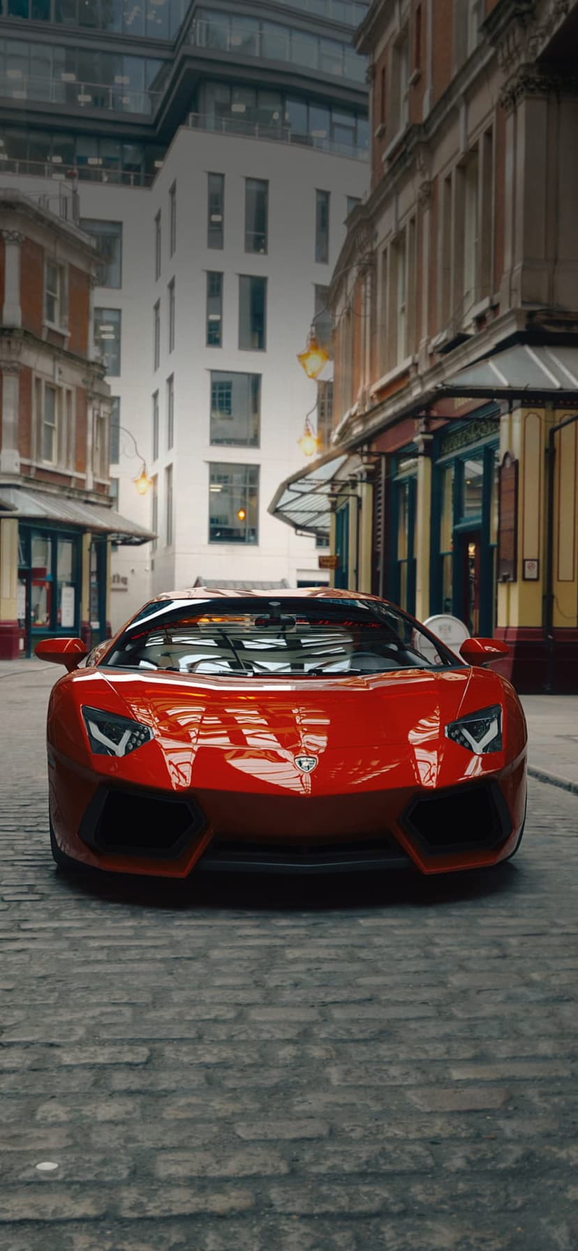 Red Lamborghini Aventador with scissor doors open parked on a stone street in front of historic city buildings.