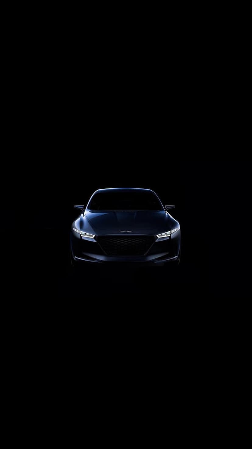 Dark luxury sedan front end shows glowing LED headlights and a lit radiator grille against deep black shadows.