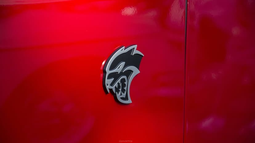 Silver and black SRT Hellcat logo badge on a glossy red car fender with soft lighting and reflections.