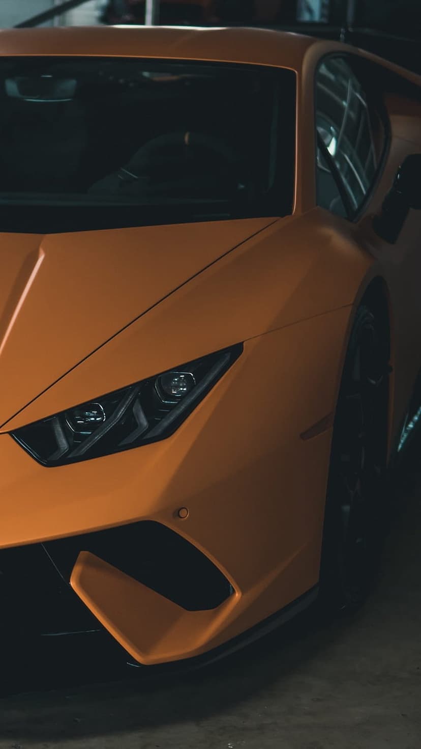Orange Lamborghini Huracan headlight showcasing intricate LED elements and sharp aerodynamic front fascia lines.