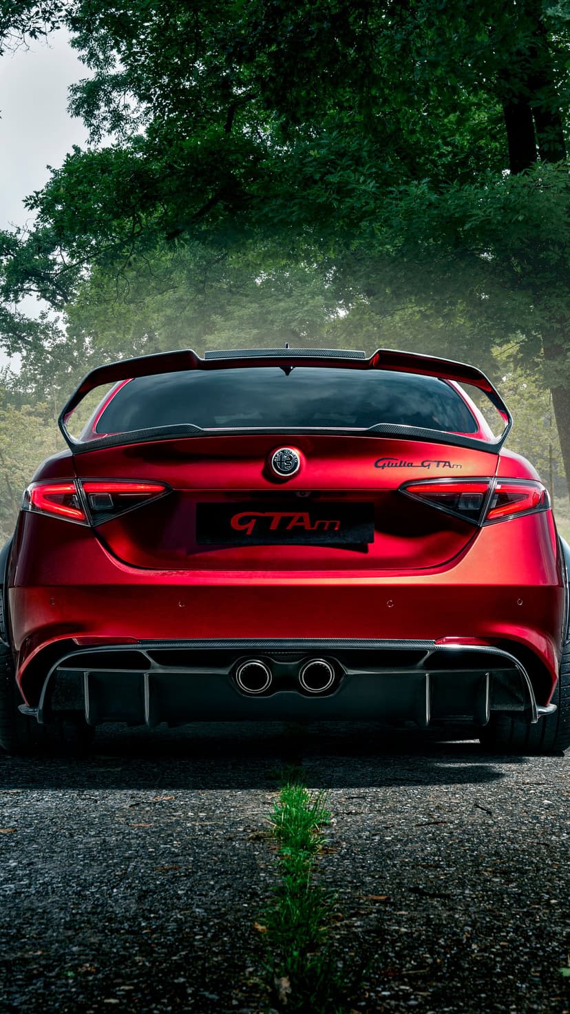 Red Alfa Romeo Giulia GTAm parked on a road with a large carbon fiber rear wing and center-exit exhausts.